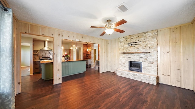 unfurnished living room with ceiling fan, a stone fireplace, and dark wood-type flooring