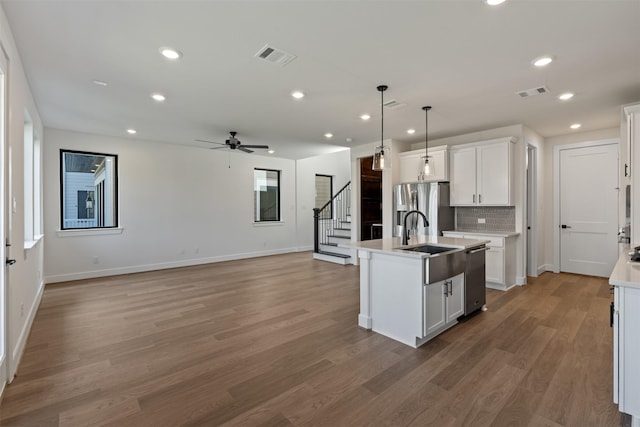 kitchen with pendant lighting, a center island with sink, white cabinets, appliances with stainless steel finishes, and wood-type flooring