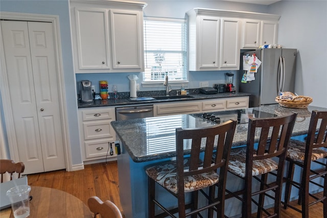 kitchen with white cabinetry, dark hardwood / wood-style flooring, dark stone counters, a kitchen bar, and appliances with stainless steel finishes