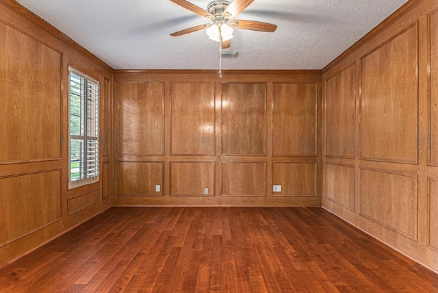 empty room featuring ceiling fan, wooden walls, dark wood-type flooring, and a textured ceiling