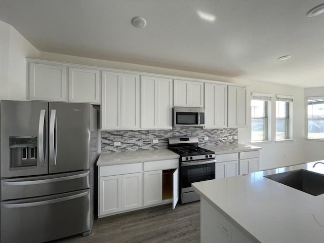 kitchen with decorative backsplash, appliances with stainless steel finishes, dark wood-type flooring, sink, and white cabinetry