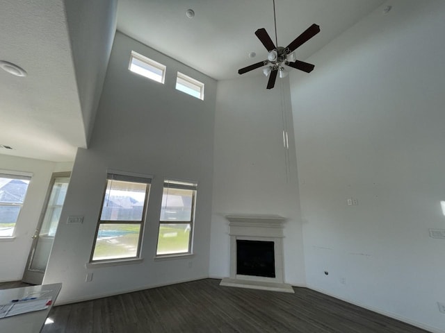 unfurnished living room with ceiling fan, plenty of natural light, dark hardwood / wood-style floors, and a high ceiling