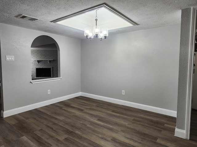 unfurnished room featuring a textured ceiling, a chandelier, a fireplace, and dark hardwood / wood-style floors