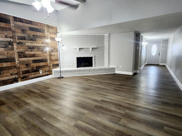 unfurnished living room with ceiling fan, dark hardwood / wood-style flooring, a fireplace, and wooden walls