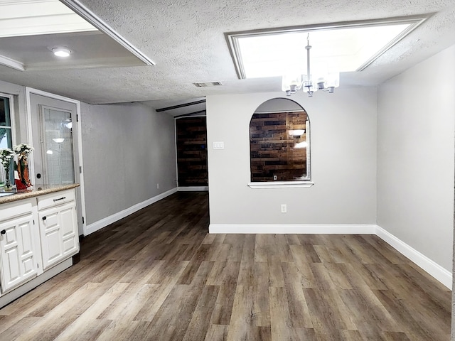 unfurnished dining area with a textured ceiling, an inviting chandelier, and dark hardwood / wood-style floors