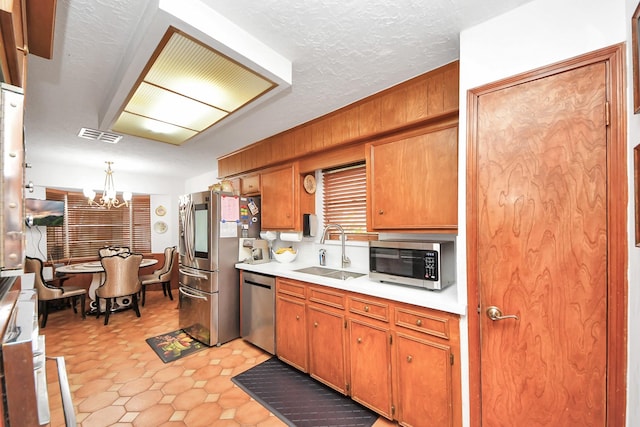 kitchen with hanging light fixtures, sink, a textured ceiling, appliances with stainless steel finishes, and a notable chandelier