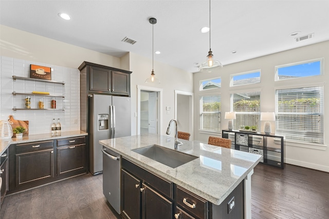 kitchen featuring sink, stainless steel appliances, backsplash, an island with sink, and decorative light fixtures