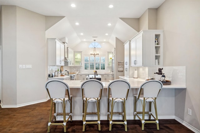 kitchen with kitchen peninsula, a kitchen bar, vaulted ceiling, dark wood-type flooring, and white cabinets