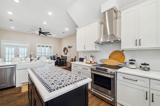 kitchen with a center island, stainless steel appliances, wall chimney range hood, tasteful backsplash, and white cabinets