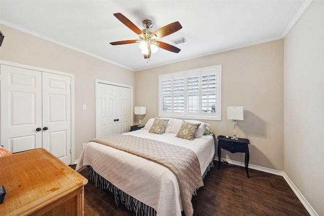 bedroom with ceiling fan, dark hardwood / wood-style flooring, crown molding, and two closets