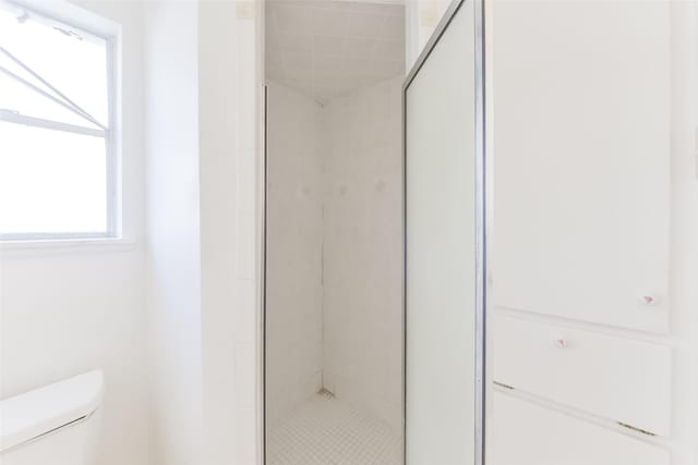 bathroom featuring a shower with door and toilet