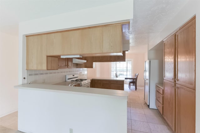 kitchen featuring white appliances, backsplash, light tile patterned floors, range hood, and kitchen peninsula