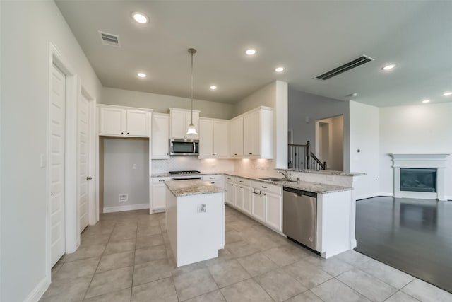 kitchen with stainless steel appliances, a kitchen island, white cabinetry, and light stone counters