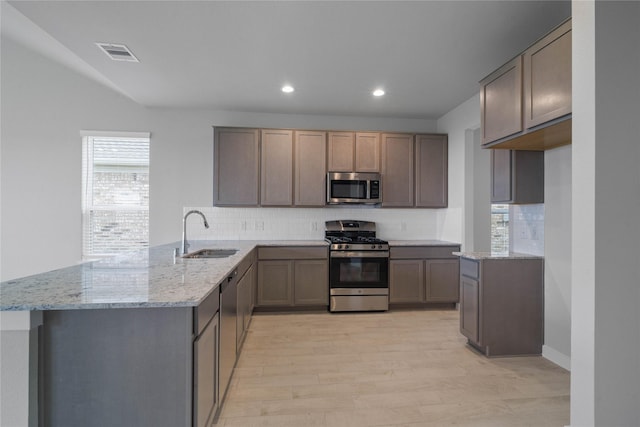 kitchen with light stone countertops, sink, kitchen peninsula, light hardwood / wood-style floors, and appliances with stainless steel finishes