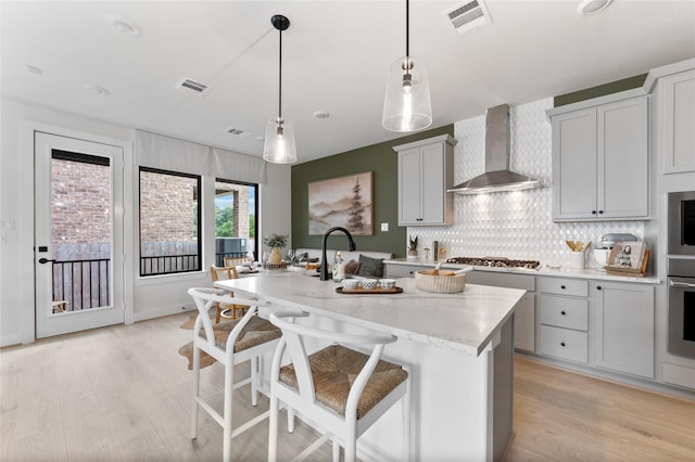 kitchen with a breakfast bar, wall chimney exhaust hood, a kitchen island with sink, and decorative light fixtures