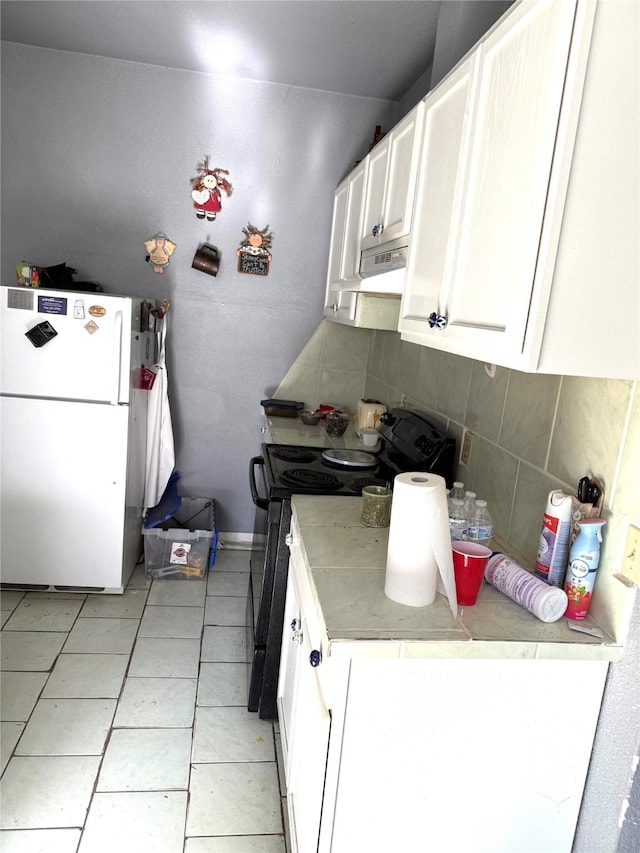 kitchen featuring black stove, tasteful backsplash, tile countertops, white fridge, and white cabinetry