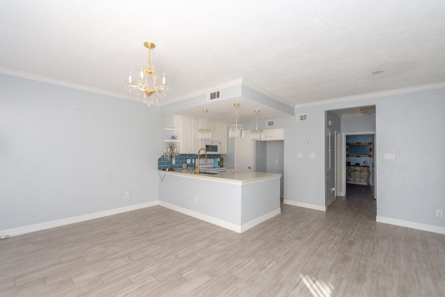 kitchen with white cabinetry, kitchen peninsula, crown molding, pendant lighting, and light hardwood / wood-style floors