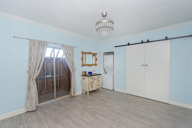 unfurnished bedroom with a barn door, ornamental molding, stacked washer and dryer, and a closet