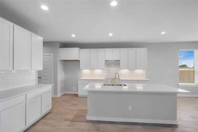 kitchen featuring white cabinets, sink, an island with sink, and light wood-type flooring