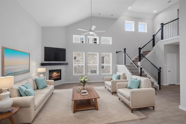 living room featuring ceiling fan, light hardwood / wood-style floors, and a towering ceiling