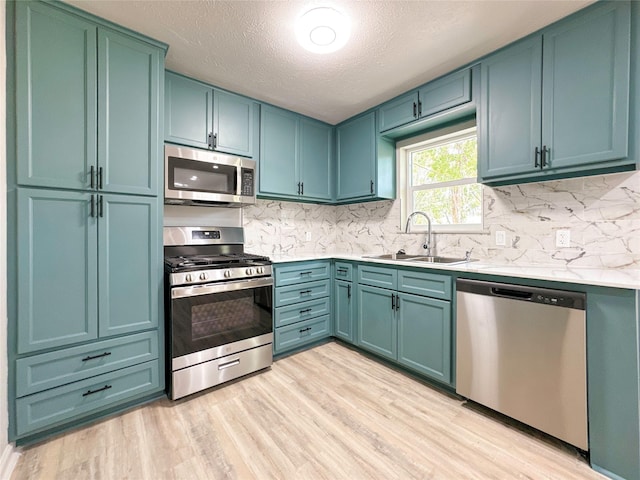 kitchen with appliances with stainless steel finishes, a textured ceiling, blue cabinets, sink, and light hardwood / wood-style floors