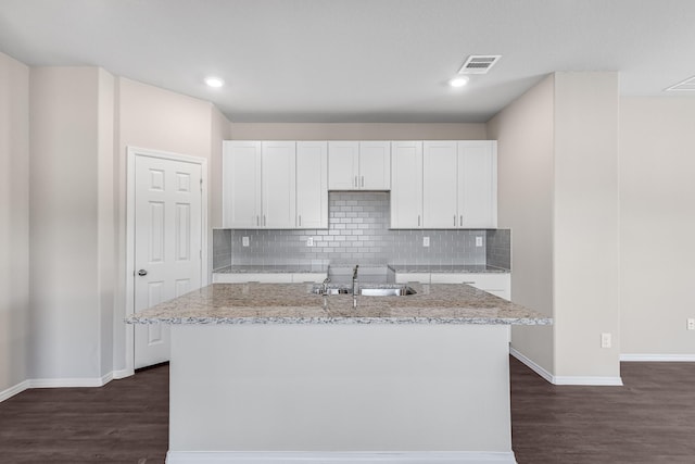 kitchen featuring a center island with sink, light stone countertops, white cabinetry, and sink