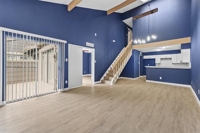 unfurnished living room with a towering ceiling, beamed ceiling, and light hardwood / wood-style floors