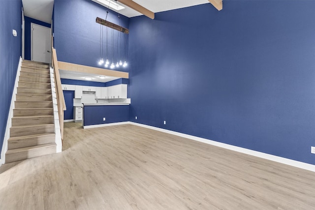 unfurnished living room with beamed ceiling, a towering ceiling, and light hardwood / wood-style floors