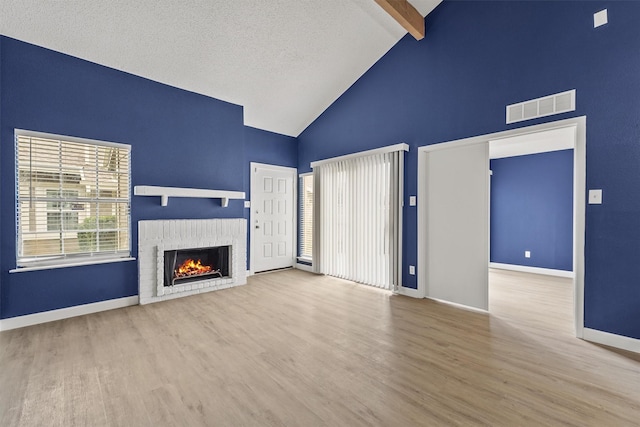 unfurnished living room featuring beamed ceiling, high vaulted ceiling, hardwood / wood-style floors, a textured ceiling, and a fireplace