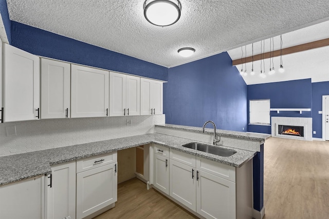 kitchen with white cabinetry, kitchen peninsula, sink, and a brick fireplace