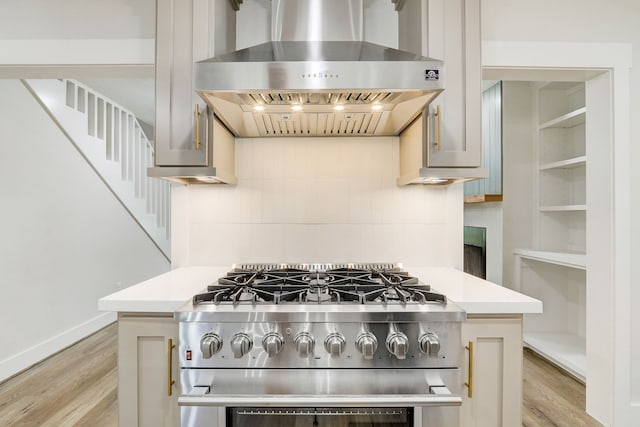 kitchen featuring high end stove, backsplash, light hardwood / wood-style flooring, and wall chimney exhaust hood