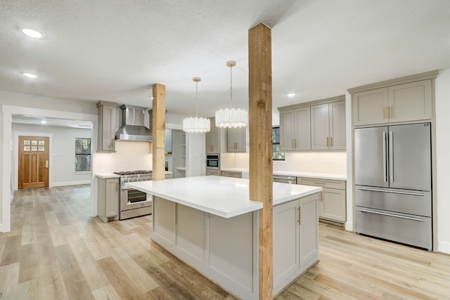 kitchen featuring appliances with stainless steel finishes, light hardwood / wood-style floors, wall chimney range hood, gray cabinets, and a kitchen island