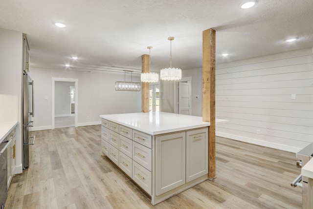 kitchen featuring stainless steel fridge, decorative light fixtures, light hardwood / wood-style flooring, a center island, and wood walls