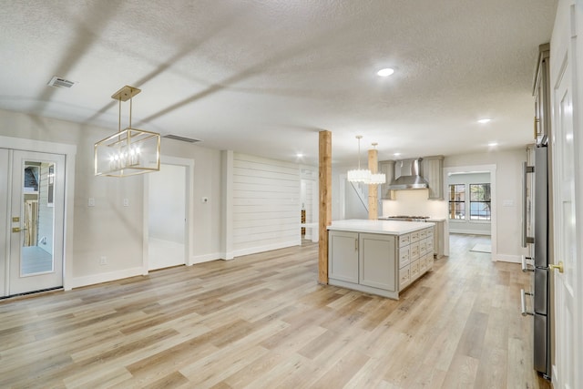 kitchen with pendant lighting, light hardwood / wood-style flooring, wall chimney exhaust hood, and a notable chandelier