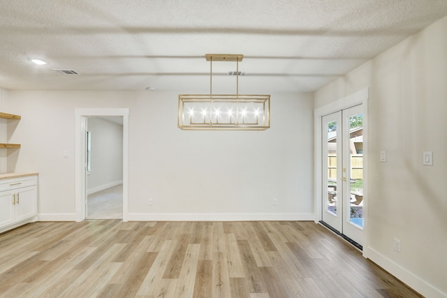 unfurnished dining area featuring french doors, a textured ceiling, and light hardwood / wood-style flooring