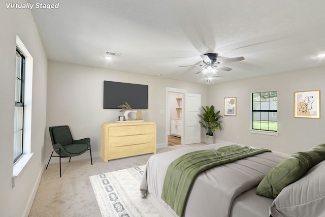 bedroom with ceiling fan, ensuite bathroom, and light carpet