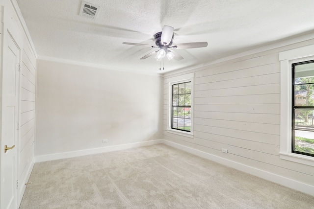 unfurnished room with a textured ceiling, light colored carpet, ceiling fan, and ornamental molding