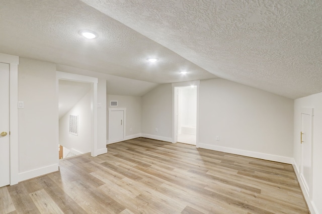 bonus room with a textured ceiling, light hardwood / wood-style floors, and lofted ceiling