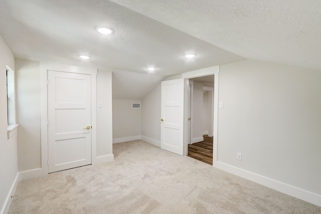 additional living space with a textured ceiling, light colored carpet, and lofted ceiling