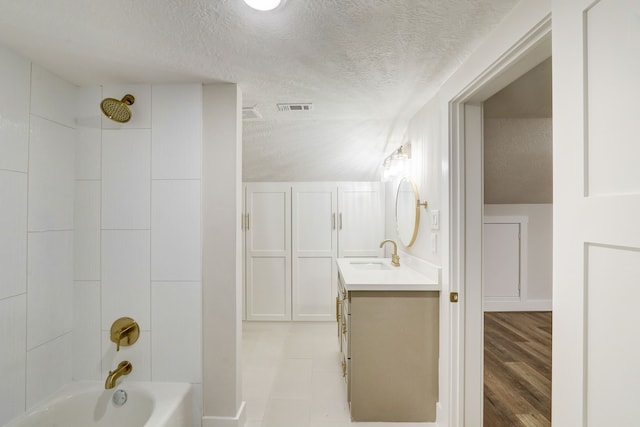 bathroom with a textured ceiling, vanity, and tiled shower / bath