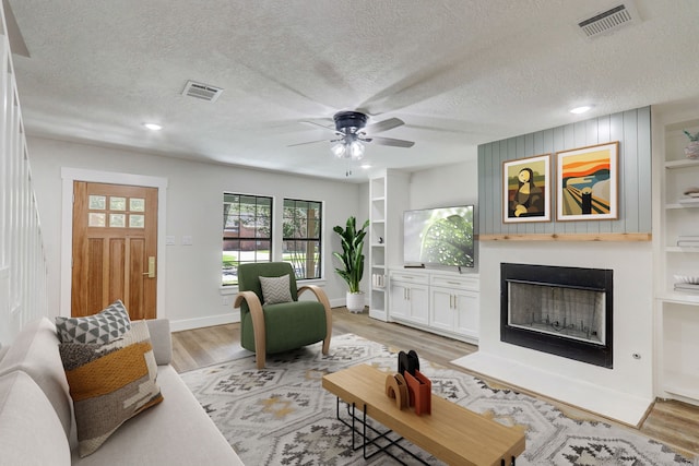 living room featuring ceiling fan, built in features, a textured ceiling, and light hardwood / wood-style flooring