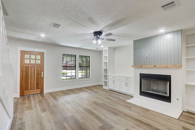 unfurnished living room featuring a textured ceiling, a large fireplace, light hardwood / wood-style flooring, and ceiling fan