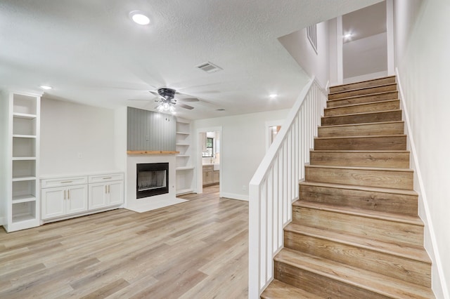 stairs with ceiling fan, a large fireplace, a textured ceiling, and hardwood / wood-style flooring