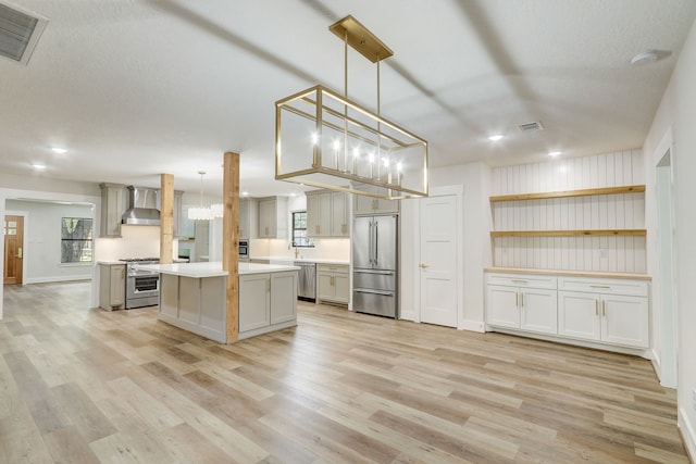 kitchen featuring light wood-type flooring, high end appliances, wall chimney range hood, a kitchen island, and hanging light fixtures