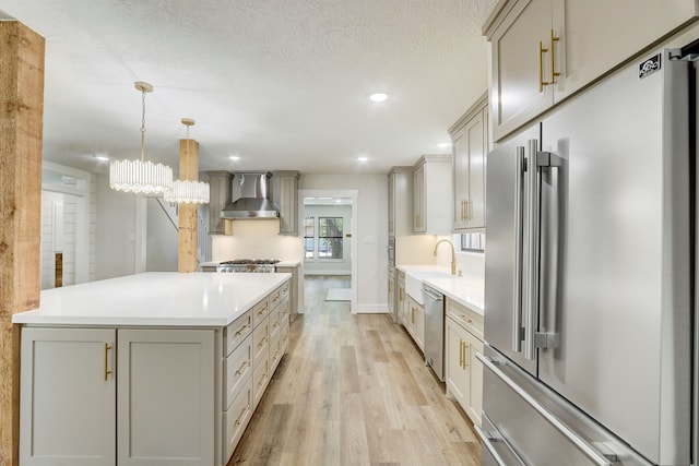 kitchen with appliances with stainless steel finishes, light wood-type flooring, wall chimney range hood, pendant lighting, and gray cabinets