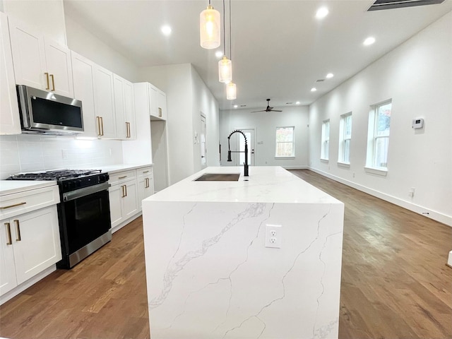 kitchen with white cabinetry, sink, hanging light fixtures, stainless steel appliances, and a center island with sink