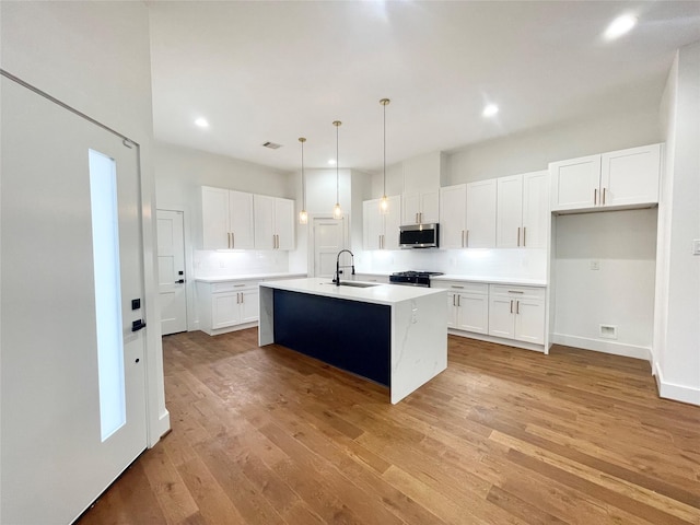 kitchen featuring a kitchen island with sink, sink, decorative light fixtures, light hardwood / wood-style floors, and white cabinetry