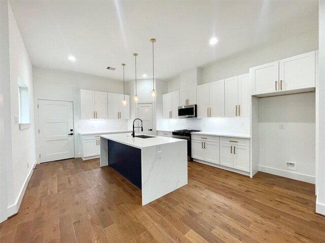 kitchen with appliances with stainless steel finishes, sink, white cabinetry, hanging light fixtures, and an island with sink