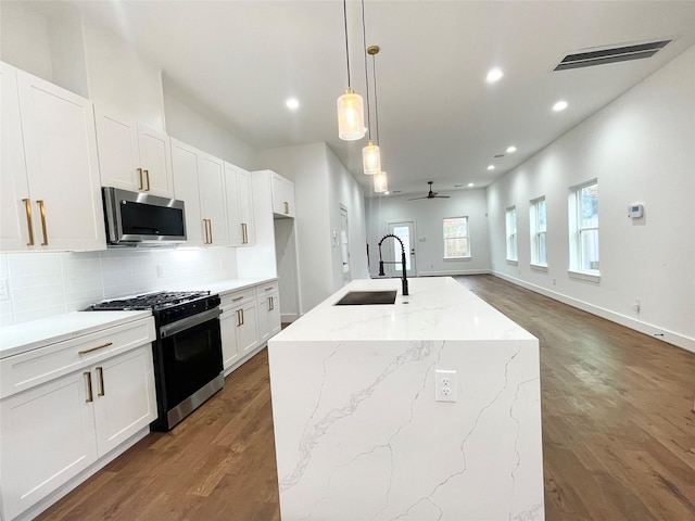 kitchen featuring sink, gas stove, hanging light fixtures, a kitchen island with sink, and white cabinets