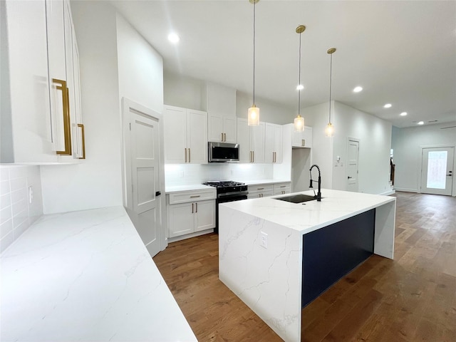 kitchen with light stone countertops, sink, a kitchen island with sink, white cabinets, and appliances with stainless steel finishes